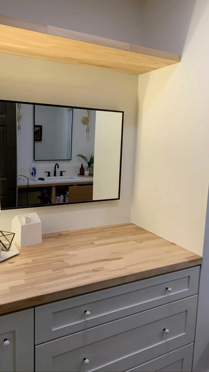 Bathroom vanity with a butcher-block top, framed mirror and open shelf above